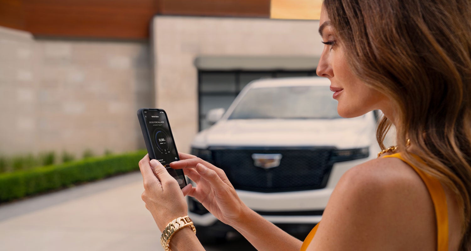 lady checking her mobile with a Cadillac vehicle background | Bayway Cadillac Southwest in Houston TX